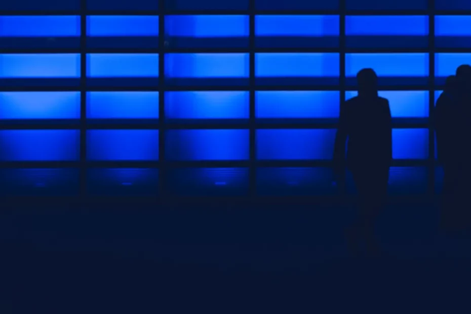 people silhoulette against glass wall lit with blue lights