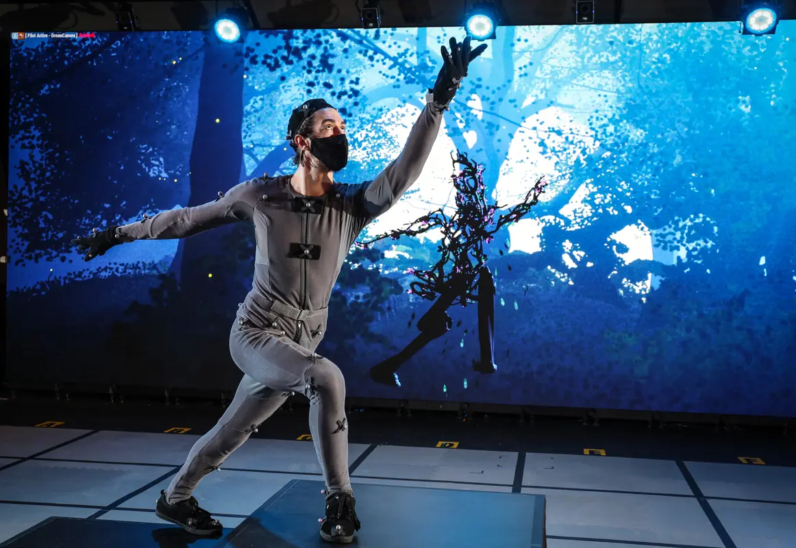 person in grey body suit moving past stage set of forest