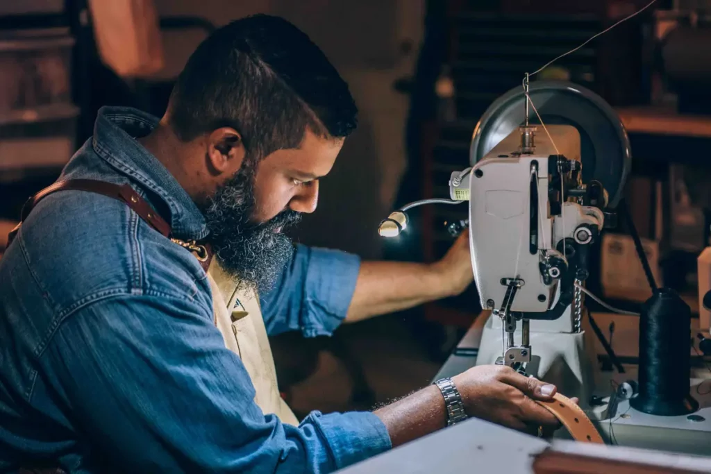 person sewing a leather belt on sewing machine