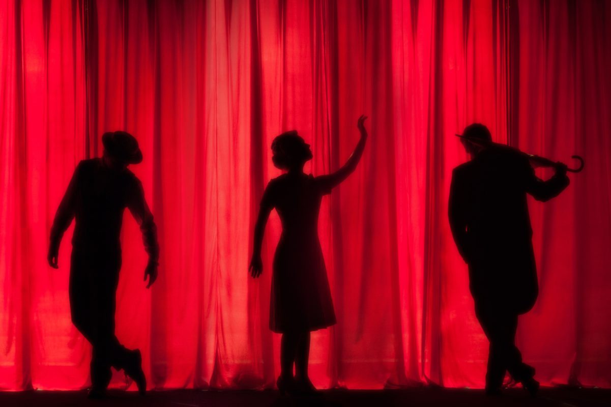 actors on stage behind a red theatre curtain